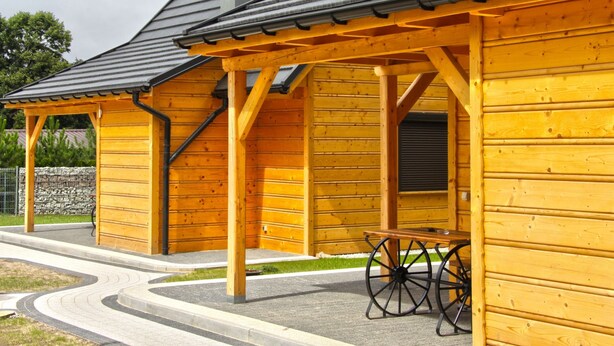 Un edificio de madera con un porche cubierto y una mesa con ruedas.
