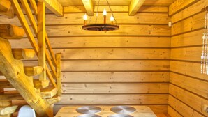 Interior de una cabaña de madera con escalera de madera, una mesa con individuales circulares y una silla blanca.