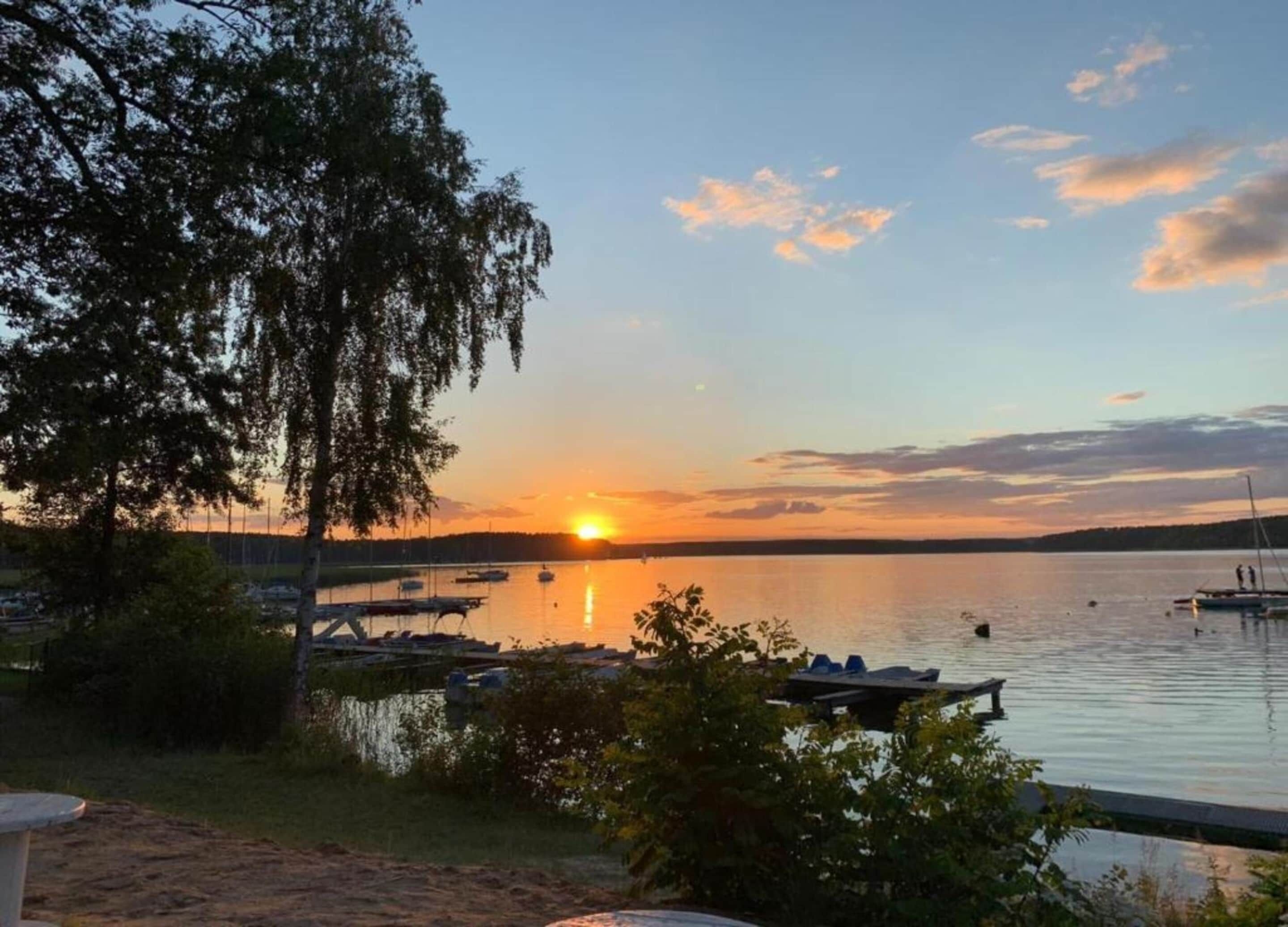A lakeside view with boats, a sunset, and a dock with chairs.