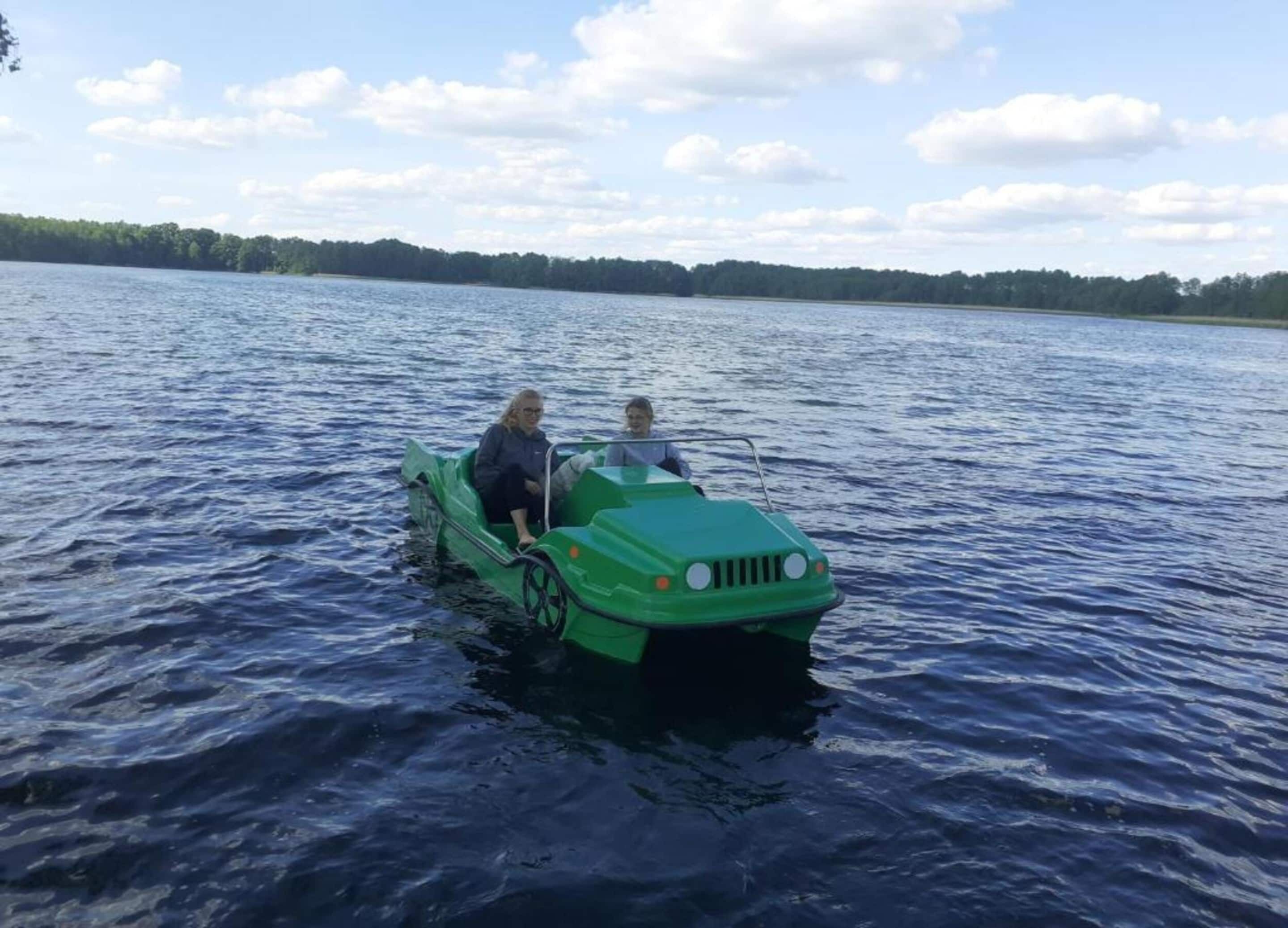 A green boat on a lake with two people on board.