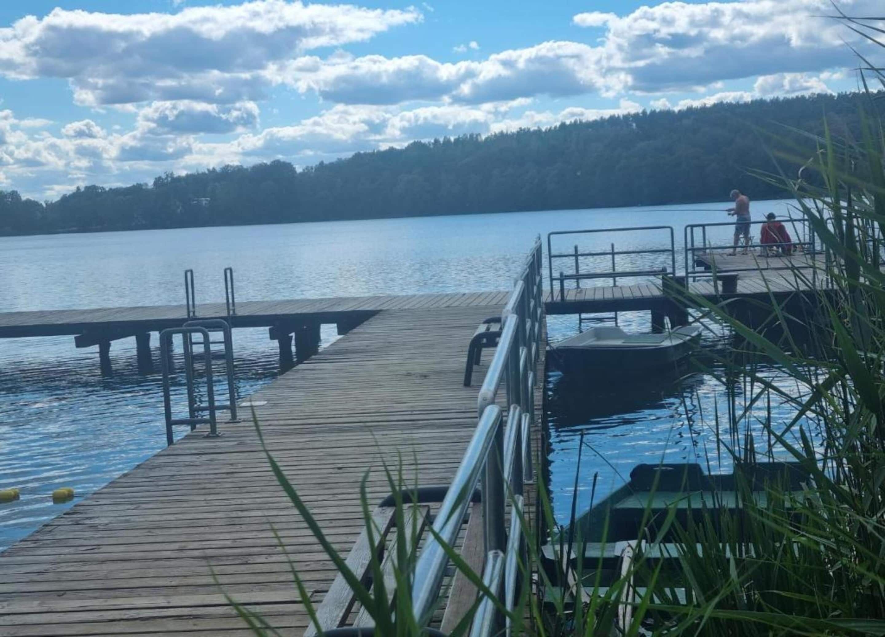 A wooden pier extending into a calm lake, with a dock and a small boat docked at the end.