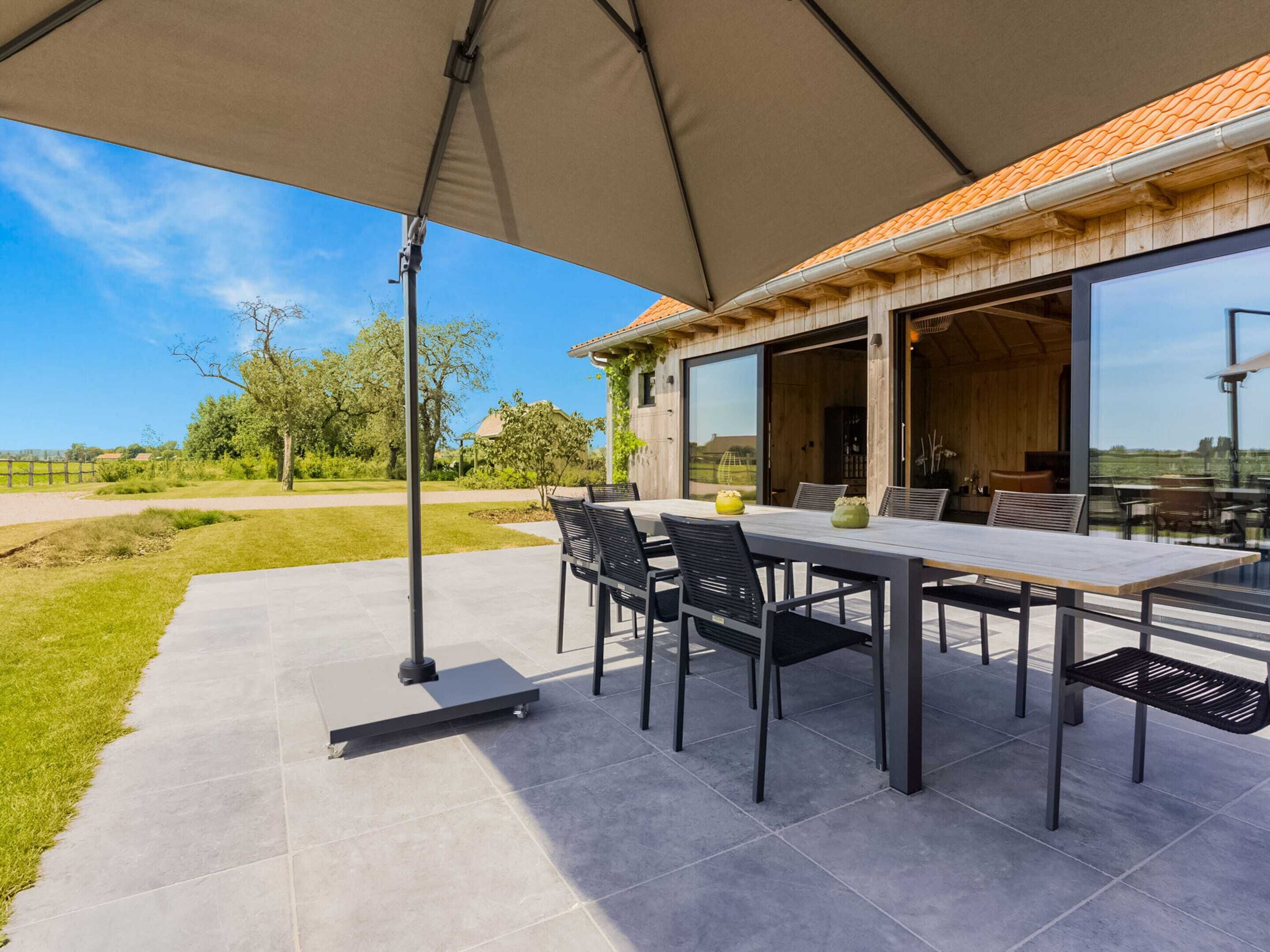 Une terrasse extérieure avec une table et des chaises, un grand parasol et une vue sur le paysage environnant.