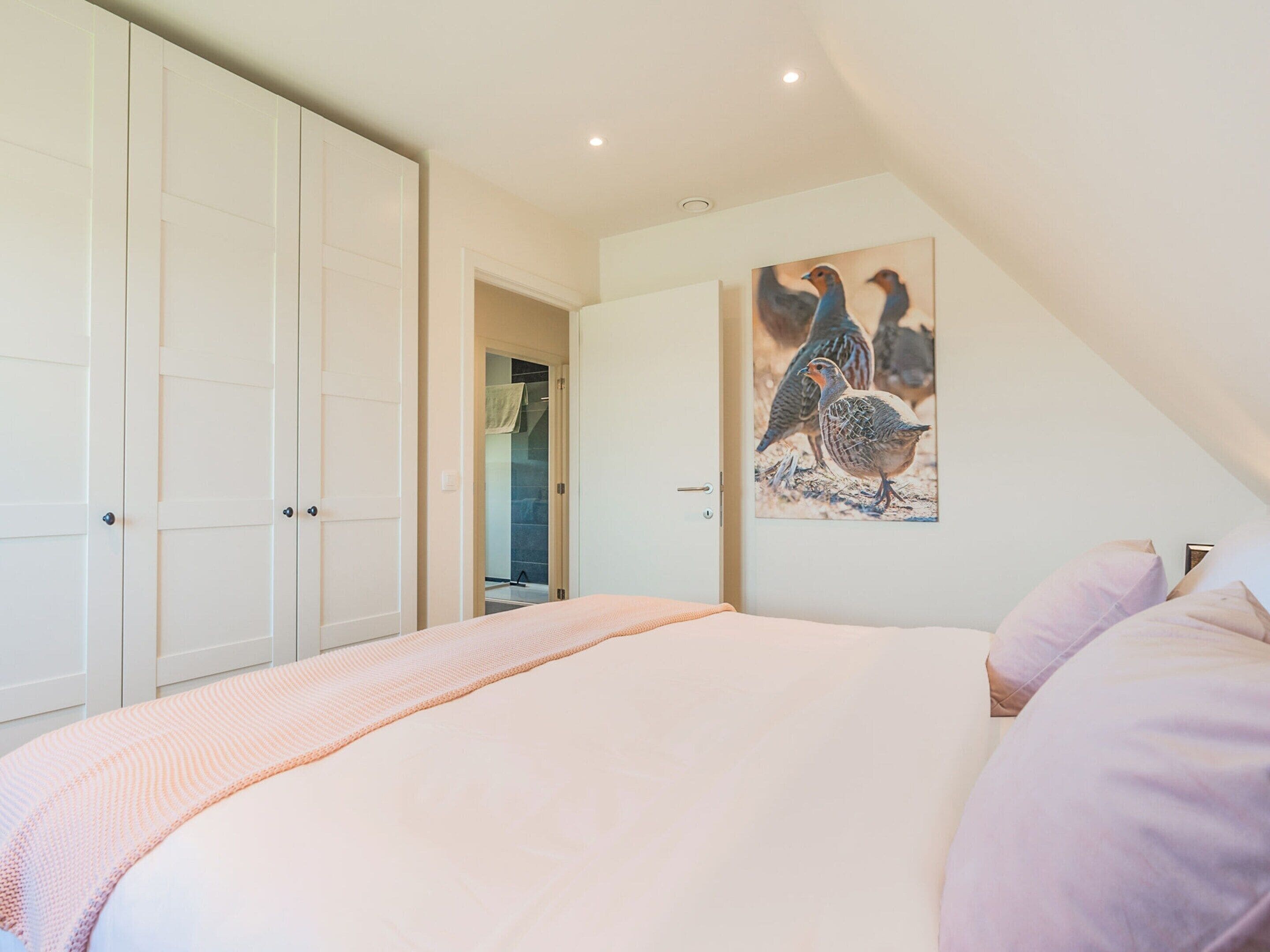 A bedroom with a large bed, a wardrobe, and a painting of birds on the wall.