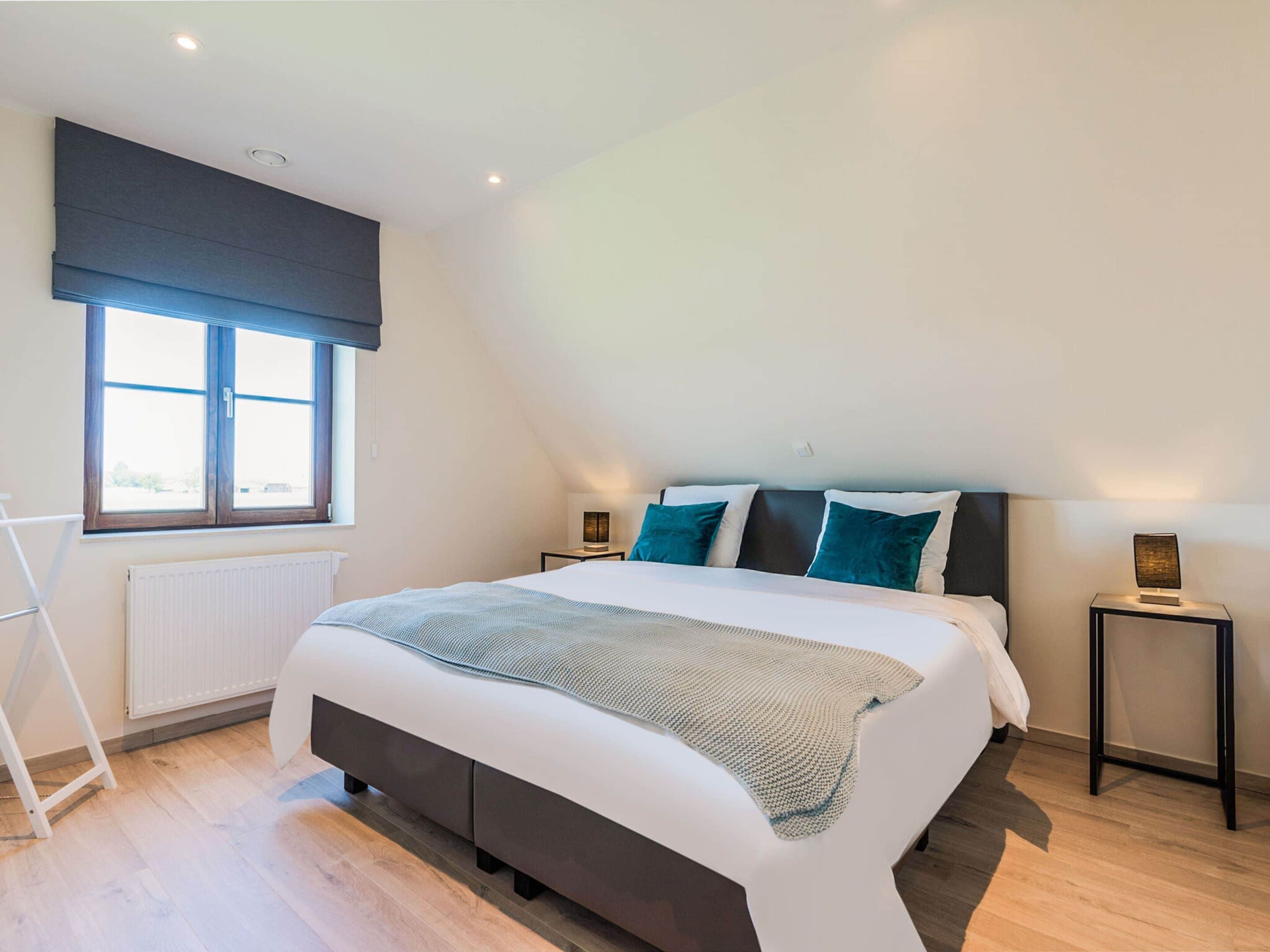 Ein modernes Schlafzimmer mit einem großen Bett, zwei Nachttischen, einem Fenster mit Jalousien und einer Heizung.