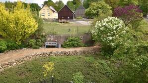 Paesaggio rurale con una casa gialla, una stalla di legno e un muro di pietra.