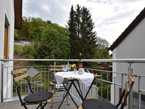 Un balcon avec une table dressée pour deux personnes, agrémentée d’une bouteille de vin Caparoz, d’un verre et d’un vase rempli de fleurs.
