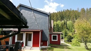 A red and grey house with a patio, outdoor seating, and a garden with planters. - Charmante Harzer Doppelhaushalfte (Osterode am Harz)