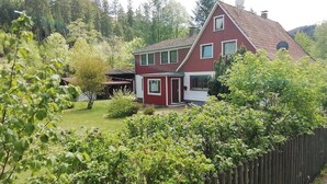 A red and white two-story house with a fenced yard and a wooden fence in the foreground. - Charmante Harzer Doppelhaushalfte (Osterode am Harz)