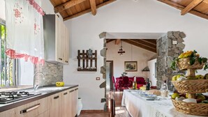 A rustic kitchen with wooden cabinets, a tiled floor, and a stone wall. - Belvilla by OYO Casa Otaiti (Maniace)
