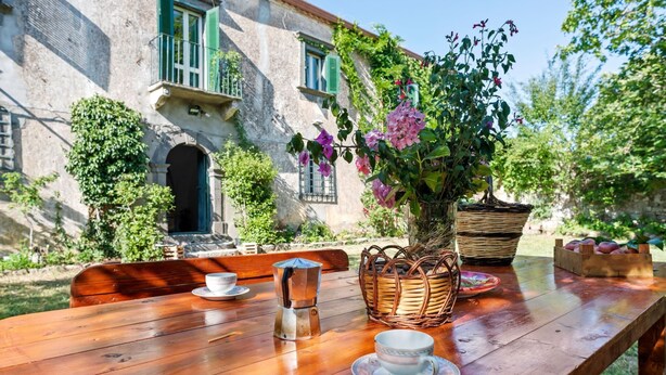 A wooden table set outdoors with a vase of flowers, a teapot, and a fruit basket. - Belvilla by OYO Casa Otaiti (Maniace)