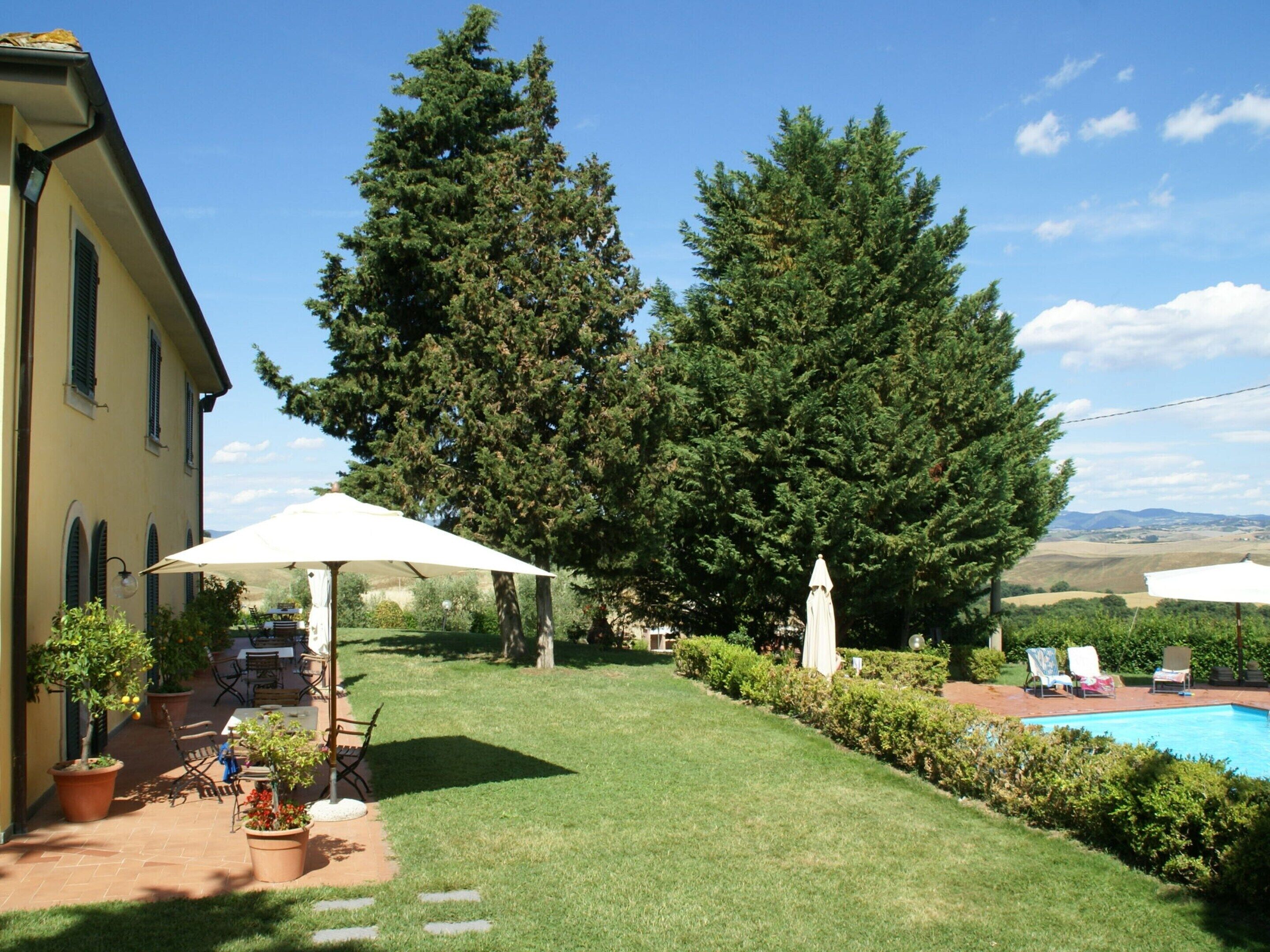 Un patio trasero con piscina, plantas en macetas y mobiliario de exterior.