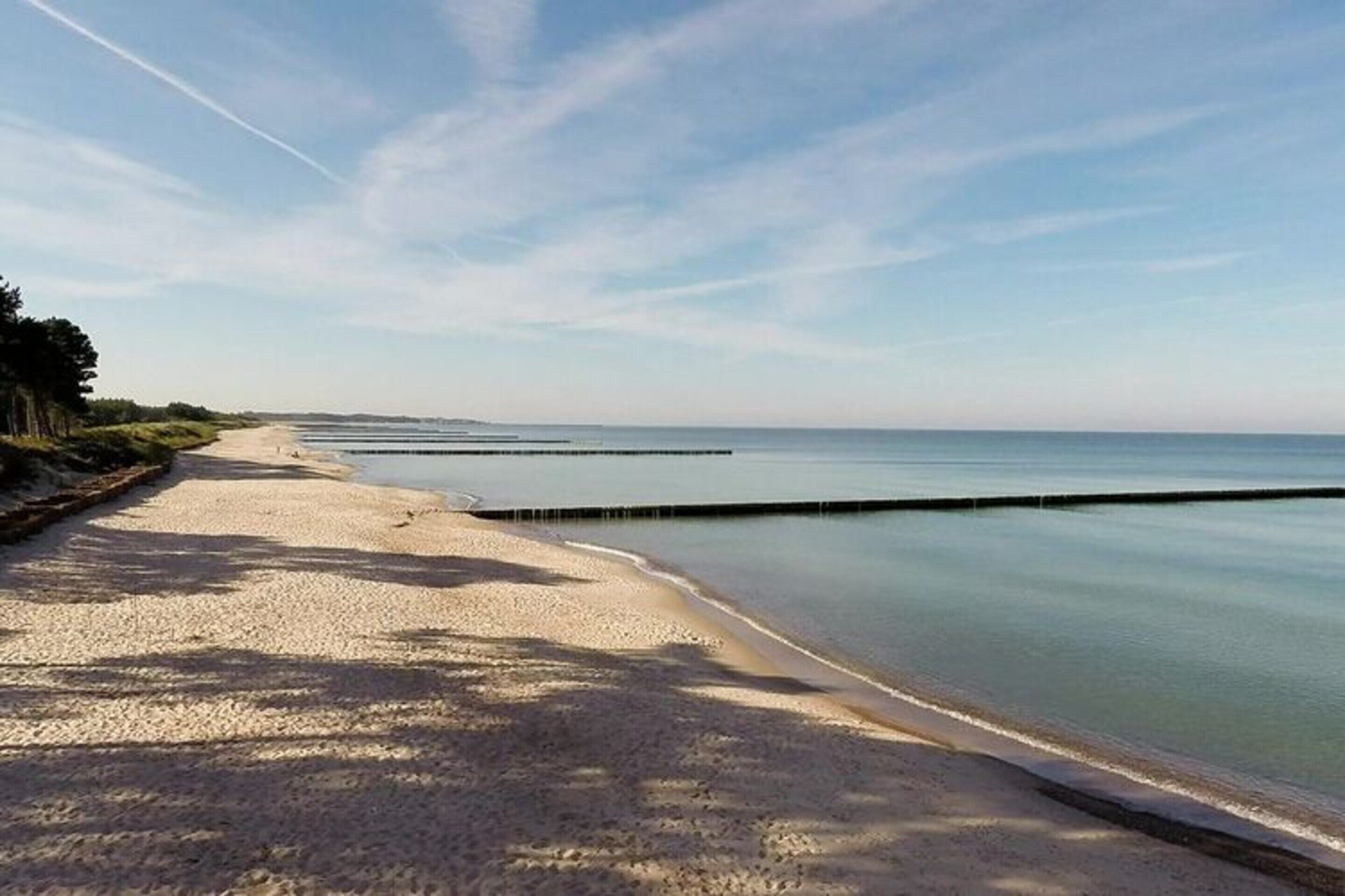 Una playa con orilla arenosa y agua tranquila, cielo despejado y un horizonte lejano.