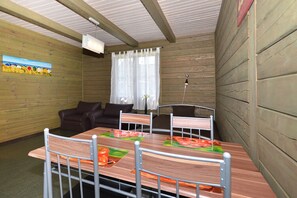 Una habitación con paneles de madera, una mesa con sillas, un sofá y un ventanal con cortinas.