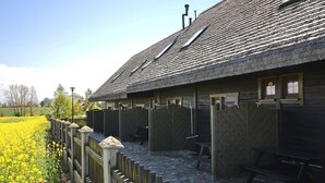 A rustic building with a sloped roof, wooden benches, and a fenced area with yellow flowers. - Cottage in Cisowo Near Baltic Coast Beach (Darlowo)