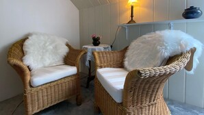 Two wicker chairs with white cushions and a small table with a vase of flowers. - Beautiful Apartment in Blankenburg With Sauna (Blankenburg)