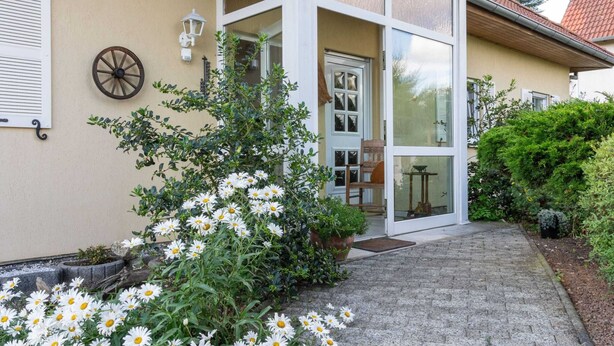 A house with a covered porch, a door with glass panels, and a wheel on the wall. - Beautiful Apartment in Blankenburg With Sauna (Blankenburg)