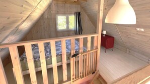 Quarto estilo loft com teto inclinado, janela com cortinas, luminária pendente branca e mesa de cabeceira vermelha.