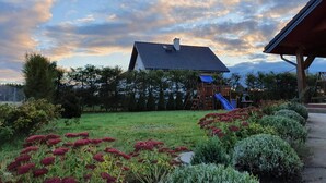Uma casa com telhado inclinado, deck de madeira e um escorrega azul.