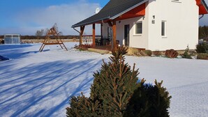 Uma casa branca com telhado vermelho e varanda coberta, cercada por neve.