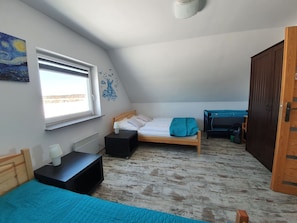 Un dormitorio pequeño y acogedor con techo inclinado, una cama individual, una mesita de noche, un aparador y una ventana con vistas.