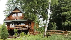 Une cabane en bois dotée d’un balcon, entourée d’arbres et bordée d’un petit étang.