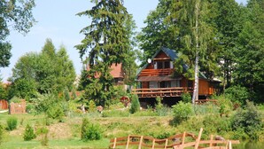 Une maison en bois dotée d’un porche donnant sur un lac paisible, entourée d’une végétation luxuriante et d’arbres.