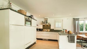 A modern kitchen with white cabinetry, a built-in oven, and a wooden dining area. - Wonderful Holiday Home nearby Efteling with Private Heated Pool & Hot Tub (Kaatsheuvel)