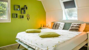 A bedroom with a green wall, a bed with white bedding, multiple pillows, a bedside table with a lamp, and a window with curtains. - Wonderful Holiday Home nearby Efteling with Private Heated Pool & Hot Tub (Kaatsheuvel)