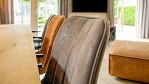 A dining area with leather chairs, a table, and a flat-screen TV mounted on the wall. - Wonderful Holiday Home nearby Efteling with Private Heated Pool & Hot Tub (Kaatsheuvel)