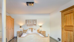 A bedroom with a wooden bed, two bedside tables with lamps, a wooden wardrobe, and a ceiling light fixture.