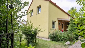 A two-story house with a yellow exterior and a red roof. There is a garden with various plants and a paved pathway leading to the entrance. - Lively Holiday Home in Wien With Private Garden (Vienna)