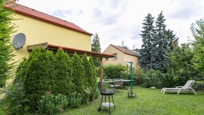 A residential backyard with a yellow house, a green lawn, a metal table with chairs, and a lounge chair. - Lively Holiday Home in Wien With Private Garden (Vienna)
