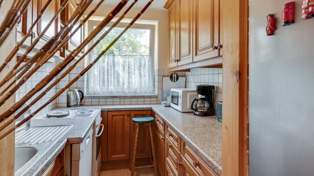 A kitchen with wooden cabinets, a microwave, a kettle, and a window with lace curtains. - Lively Holiday Home in Wien With Private Garden (Vienna)