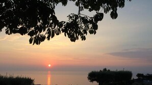 A sunset over a body of water with a view of a grassy area and some trees. - Apartment in Gasponi With Mountain Views (Drapia)