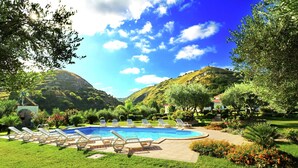 A swimming pool with lounge chairs, surrounded by well-maintained grass and flowers, with hills in the background. - Apartment in Gasponi With Mountain Views (Drapia)