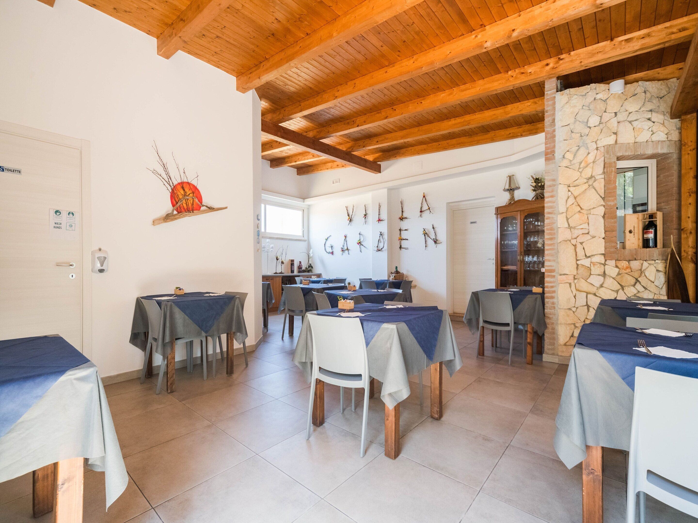 A dining area with tables set for guests, a stone wall, and a wooden ceiling.