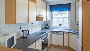 A modern kitchen with wooden cabinets, a built-in oven, a kettle, and a window with a view. - Chalet mit Sauna und Sommergastekarte Zell am See (Zell am See)