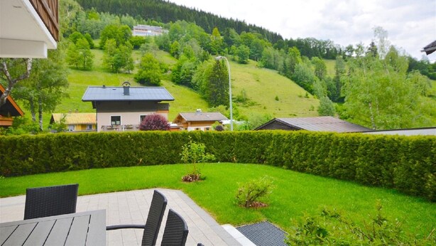 A residential area with a view of a green hill and a house with a dark roof. - Chalet mit Sauna und Sommergastekarte Zell am See (Zell am See)