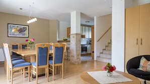 A modern living room with a dining area, a staircase, and a kitchen in the background. - Chalet mit Sauna und Sommergastekarte Zell am See (Zell am See)