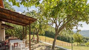 A covered outdoor seating area with tables and chairs, surrounded by trees and a fenced view of a hilly landscape. - Holiday Home in Tuscany With Private Garden (Pieve Santo Stefano)