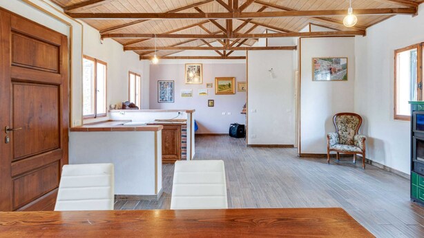 A spacious kitchen with a wooden ceiling, a dining area with a wooden table, and a living area with a chair and a fireplace. - Holiday Home in Tuscany With Private Garden (Pieve Santo Stefano)