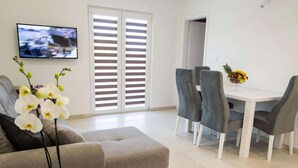 A modern living room with a grey sofa, a dining table with four chairs, and a TV mounted on the wall. - Plush Apartment in Imotski near Blue & Red Lakes (Imotski)