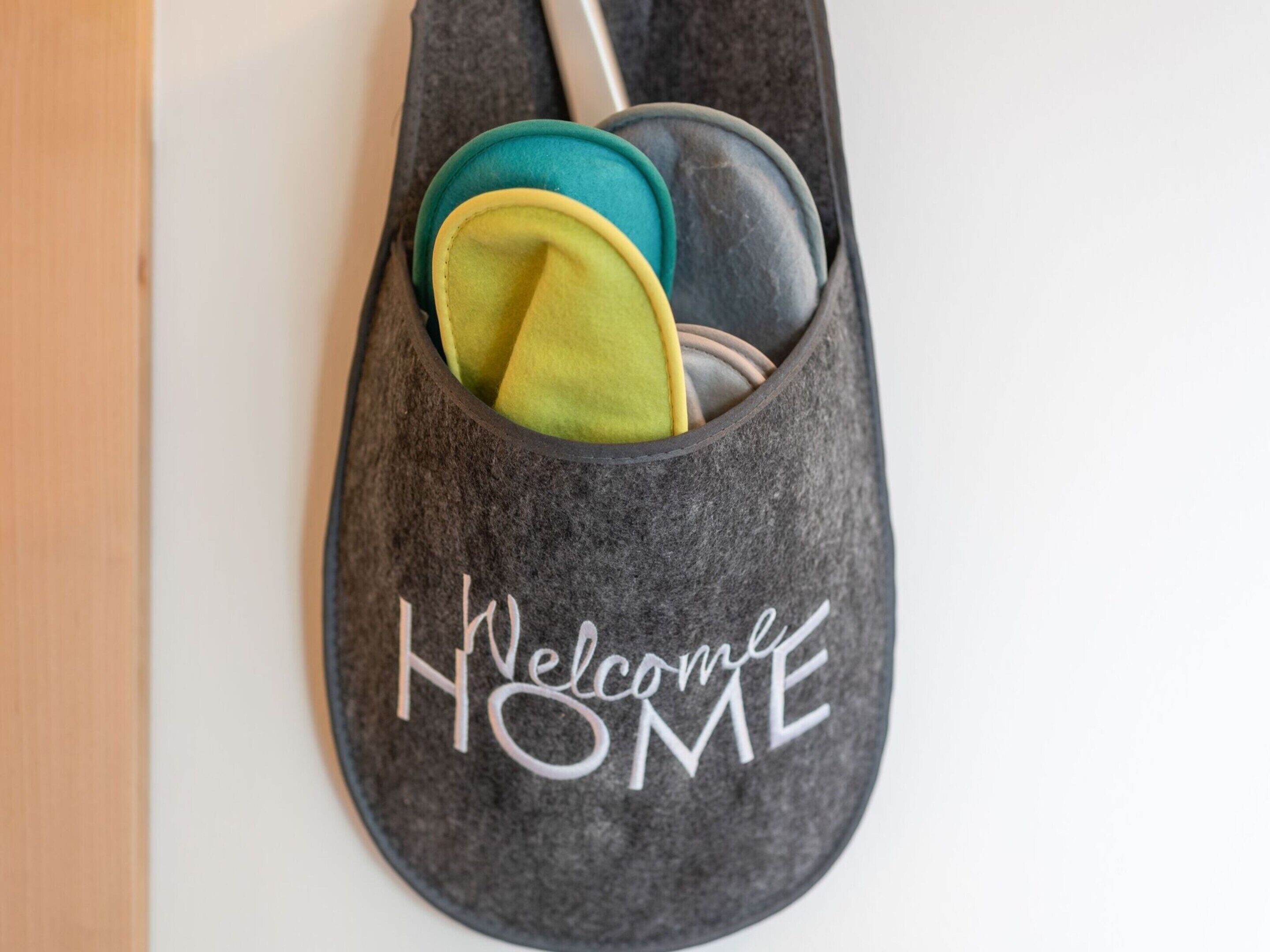 A gray felt slipper with a "Welcome HOME" inscription, containing a pair of green and yellow slippers.
