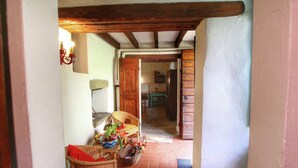 A narrow hallway with a tiled floor, wooden beams on the ceiling, and a wicker chair with a red cushion. - Belvilla by OYO Casina del Forno (Rufina)