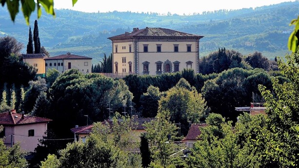 A large, two-story building with a symmetrical facade, surrounded by lush greenery and hills in the background. - Belvilla by OYO Casina del Forno (Rufina)