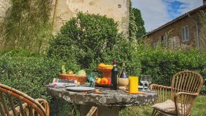 An outdoor dining table with a basket of fruits, a bottle, and a chair in front of a rustic building. - Belvilla by OYO Casina del Forno (Rufina)
