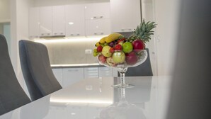 Eine moderne Küche mit weißen Schränken und einem Glastisch, auf dem sich eine Obstschale befindet.