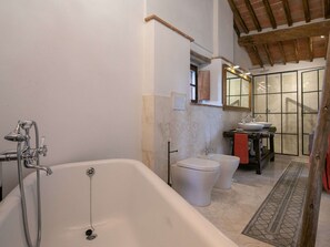 Een badkamer met een bad, twee toiletten, een wastafel en een douche.