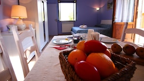 A room with a dining table set for two, a basket of fruit, and a bed with a blue bedspread. - Farmhouse in Casperia With Pool & Scenic Views (Casperia)