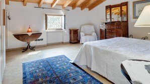 Quarto com teto de madeira, uma cama, uma cadeira, escrivaninha com luminária e uma janela.